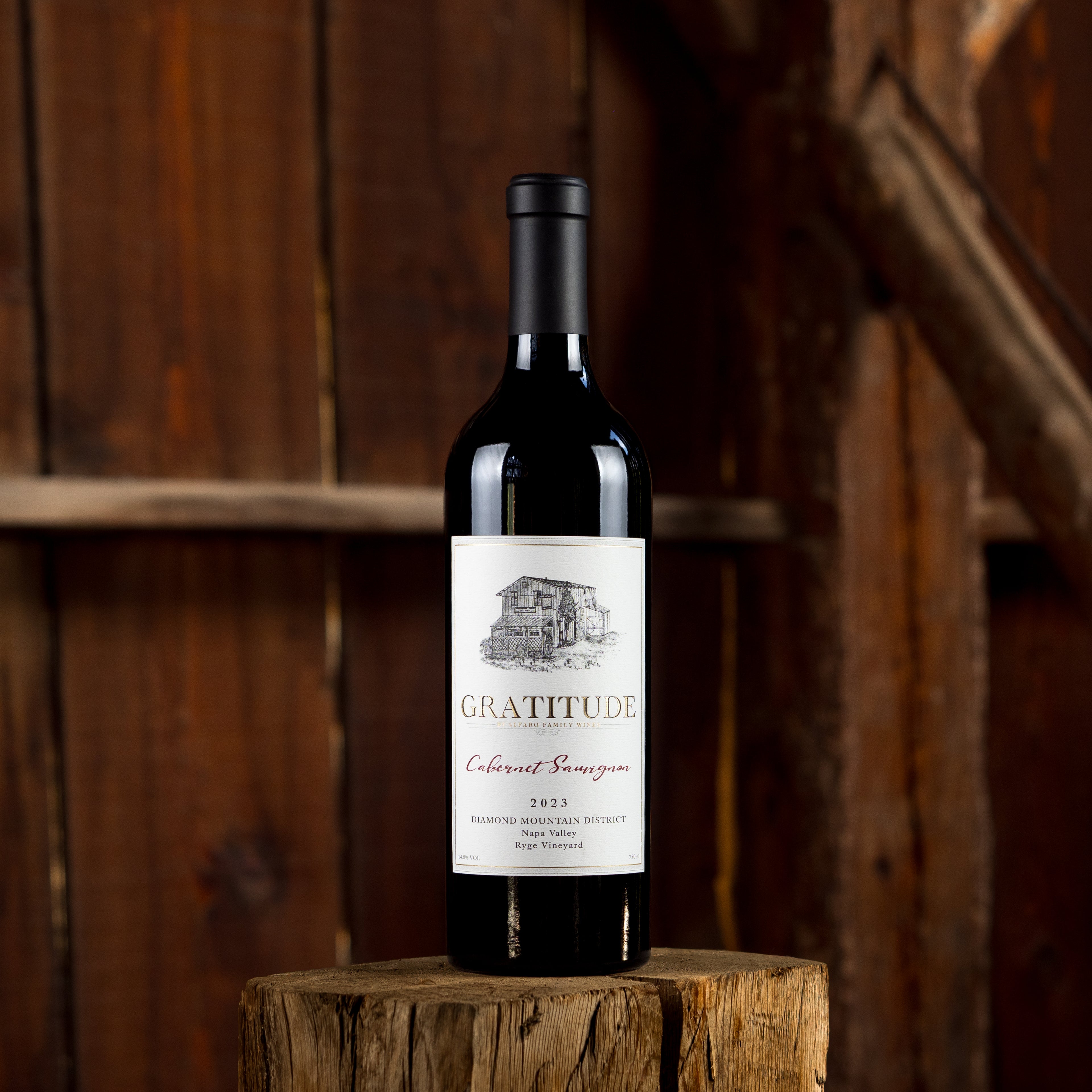 Wine bottle labeled 'Gratitude' on a wooden stump with wooden barn background